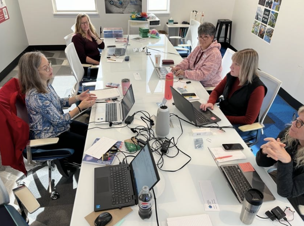 Educators sit around a long conference table, each with a laptop and Micro:bit materials. 